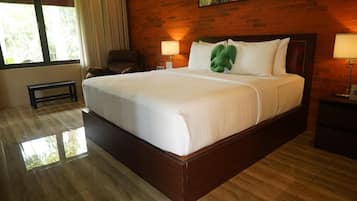 A hotel room with a large bed, a wooden headboard, a nightstand with a lamp, a chair, and a window with curtains.