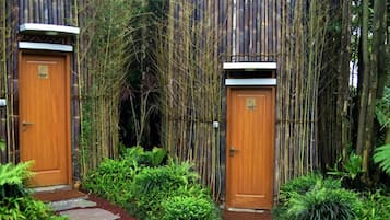 Two wooden doors with a bamboo fence and a stone pathway leading to them.
