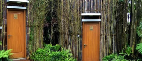 Two wooden doors with a bamboo fence and a stone pathway leading to them.