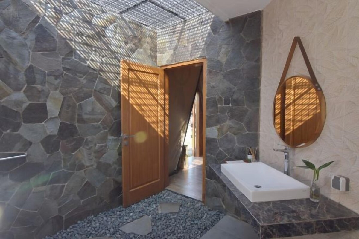 A bathroom with a stone wall, a wooden door, a white sink, and a round mirror.