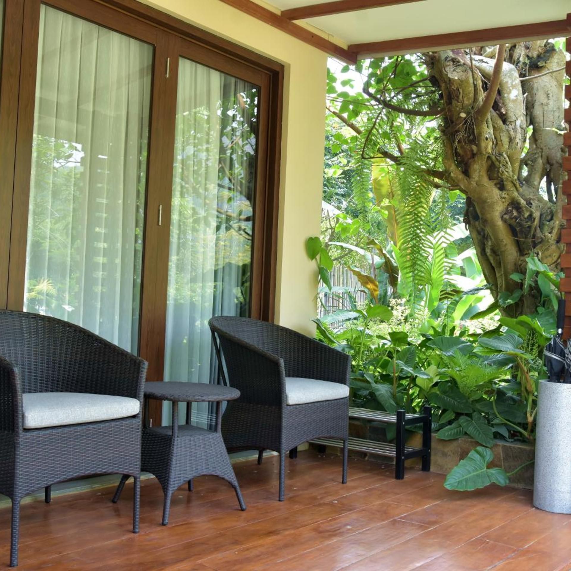 Un patio techado con mobiliario de mimbre, un árbol grande y vistas a un jardín exuberante.