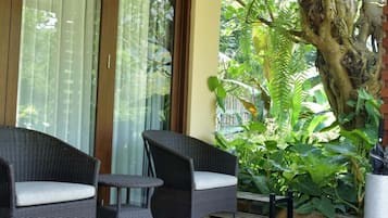 Un patio techado con mobiliario de mimbre, un árbol grande y vistas a un jardín exuberante.