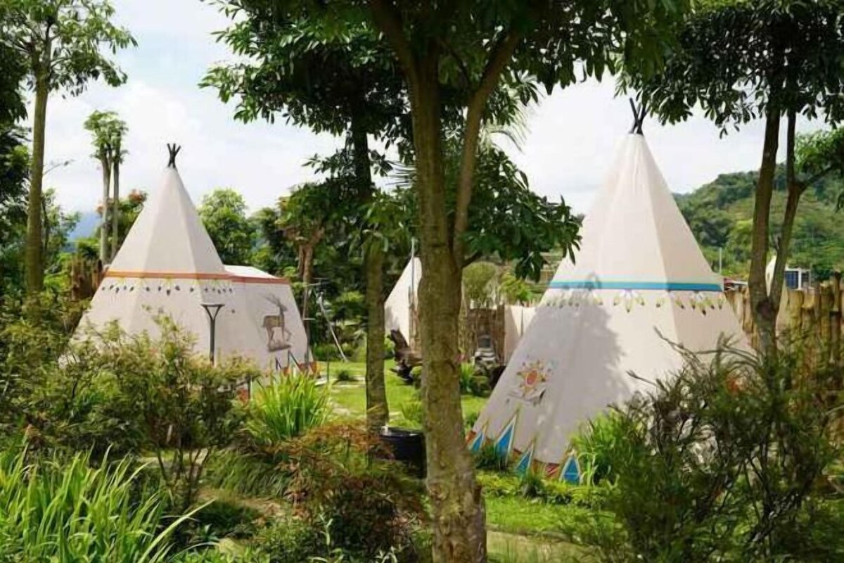 A campsite with several conical tents, surrounded by trees and greenery.