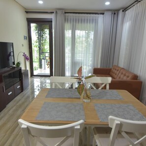 Una sala moderna con un sofá, una mesa de comedor con sillas, un televisor y un balcón con plantas.