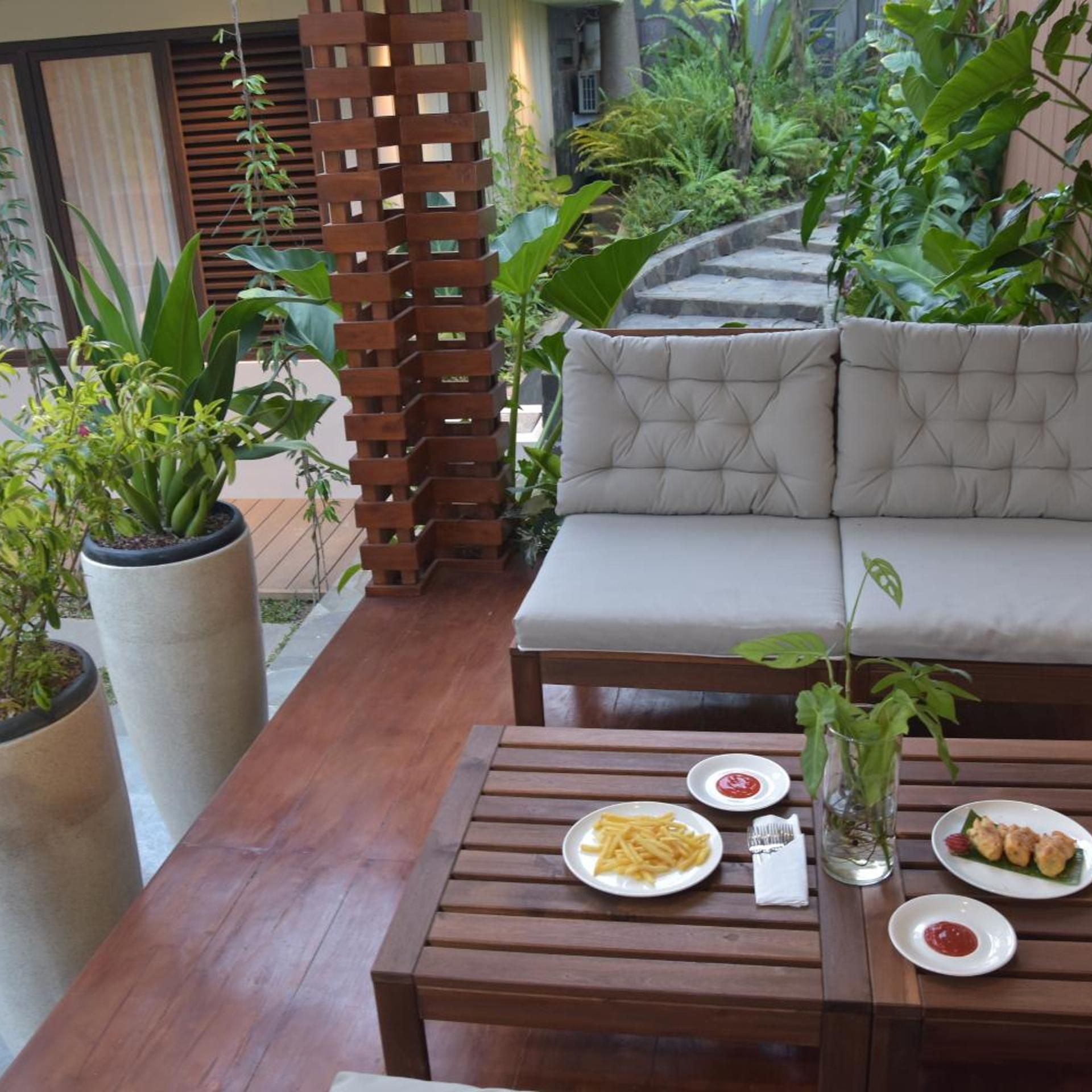 An outdoor seating area with a wooden table, a cushioned sofa, and potted plants.