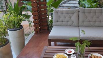 An outdoor seating area with a wooden table, a cushioned sofa, and potted plants.