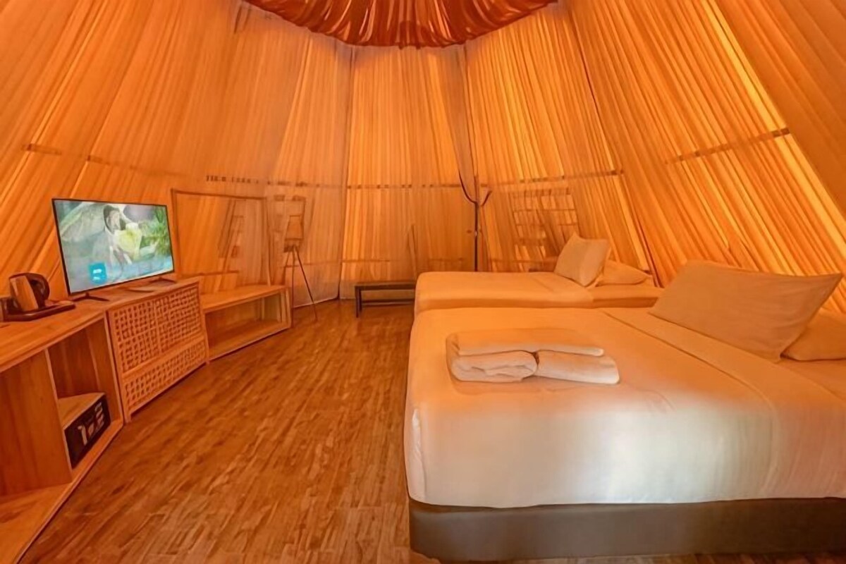 Una habitación tipo tienda con cama, televisión y mesita de madera.