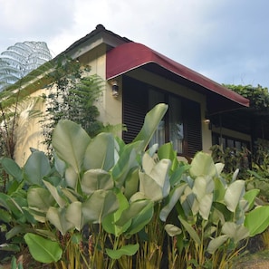 A modern house with a red roof, surrounded by lush greenery and large leaves. - Sarga Earthing Resort (Cipanas)