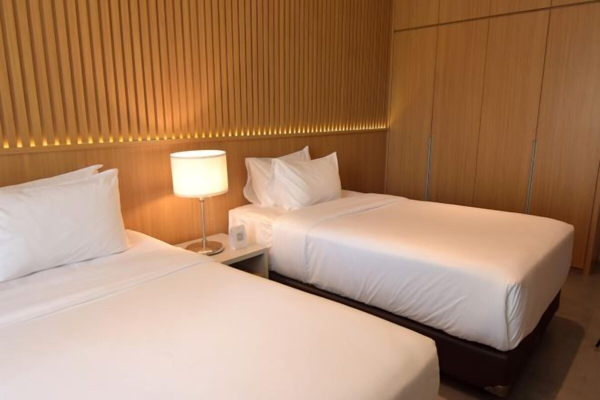 A hotel room with two single beds, a bedside table with a lamp, and a wooden panel wall.