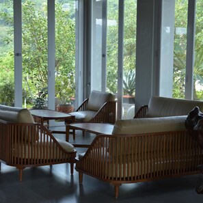 A room with large windows, a sofa, a table, and chairs. - Sarga Earthing Resort (Cipanas)