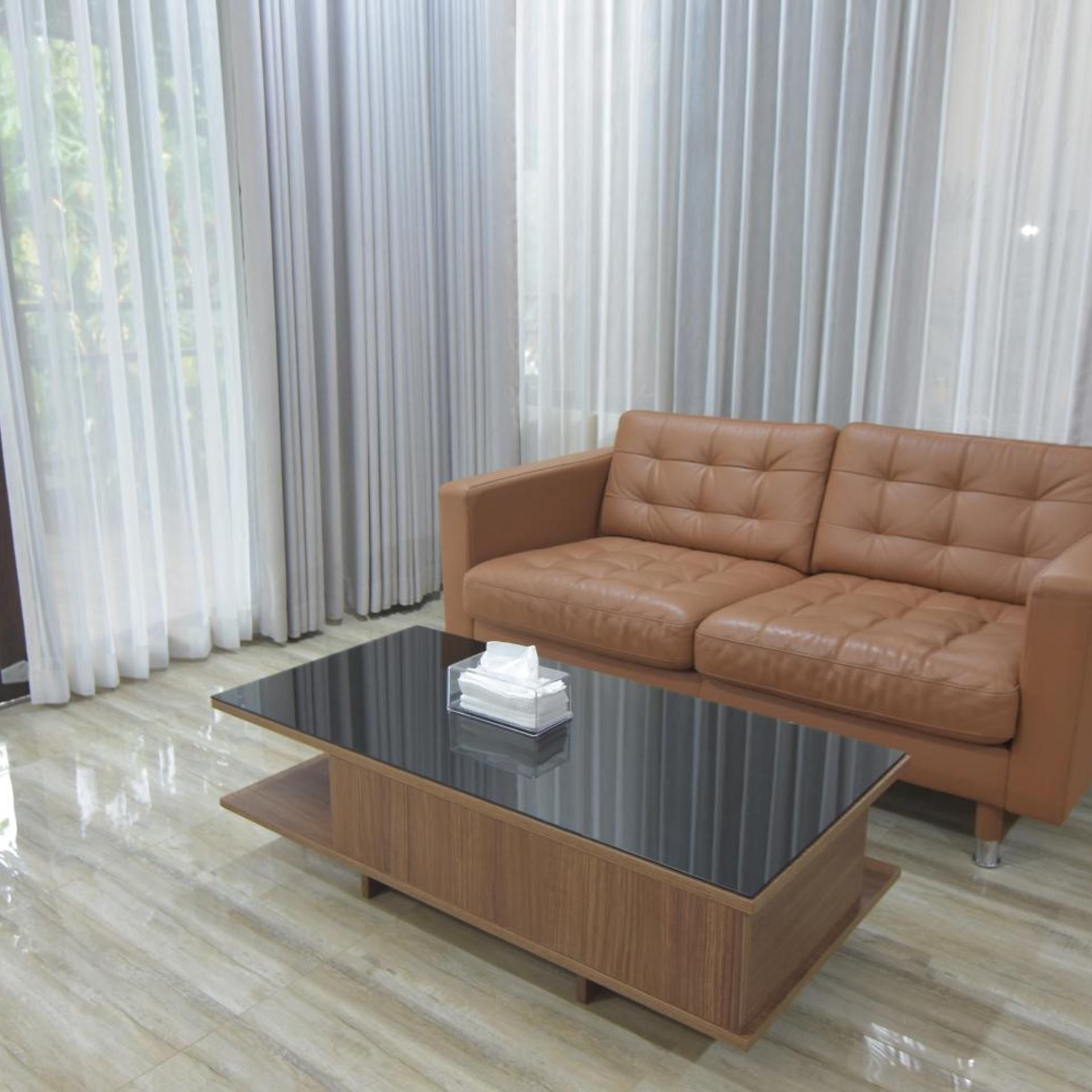 Una sala moderna con un sofá de cuero, una mesa de centro de vidrio y vistas a través de cortinas traslúcidas.