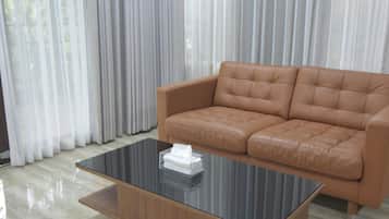 Una sala moderna con un sofá de cuero, una mesa de centro de vidrio y vistas a través de cortinas traslúcidas.