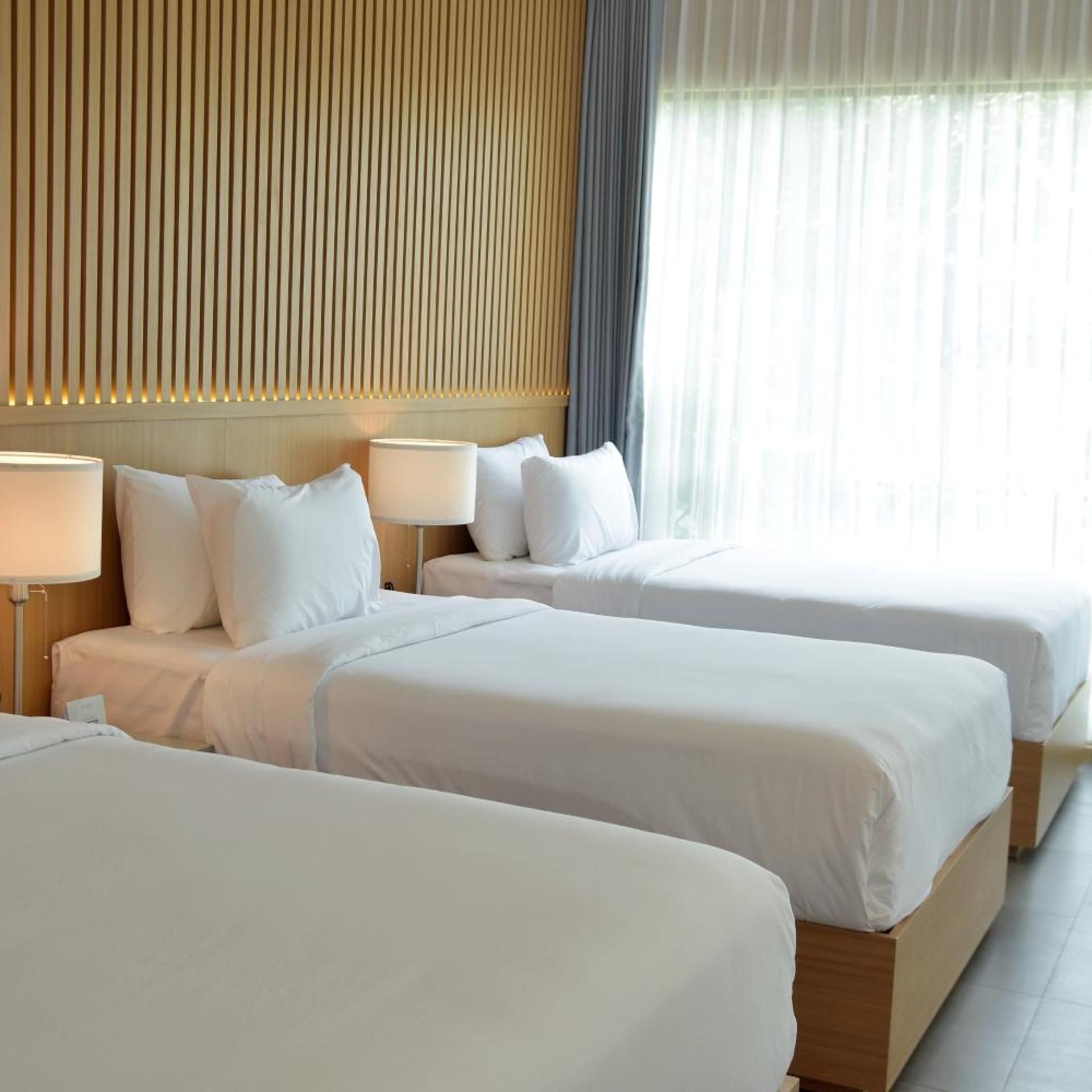Hotellihuone, jossa on kaksi sänkyä, puinen pääty ja suuri ikkuna, jossa on verhot.