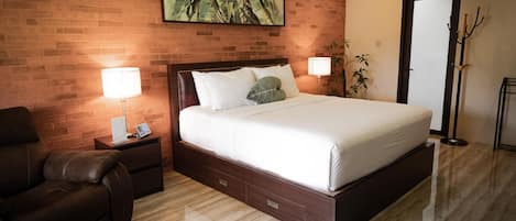 A hotel room with a brick wall, a large bed, a nightstand, a leather chair, and a floor lamp.