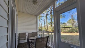 A covered porch with a table and chairs, a white railing, and a view of trees and grass. - River Oaks Condo, King Suite, Pools & Hot Tub (Myrtle Beach)