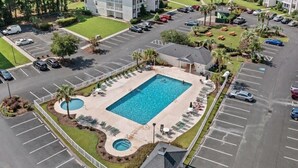 An aerial view of a hotel with a swimming pool, multiple parking lots, and surrounding greenery. - River Oaks Condo, King Suite, Pools & Hot Tub (Myrtle Beach)