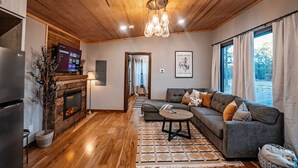 A modern living room with a wooden ceiling, a grey sofa, a small round table, and a fireplace.