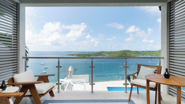 A balcony with a view of the sea, wooden furniture, and a small table. - Luxe Condo, Ocean Views and pool (St. George)