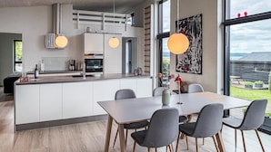 Una cucina moderna con isola centrale, tavolo da pranzo con sedie, lampade a sospensione e un'ampia finestra vista panoramica.