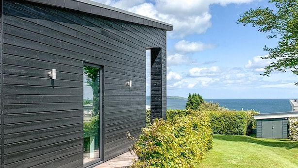 Una casa moderna con facciata scura, ingresso con porta in vetro e vista sul mare.