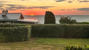 Una casa con pannelli solari sul tetto, un siepe curata e vista sul mare al tramonto.