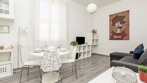 A modern living room with a dining area, a grey sofa, a white table, and a painting on the wall. - Coliseum View Diana's House by Rentbeat (Roma)