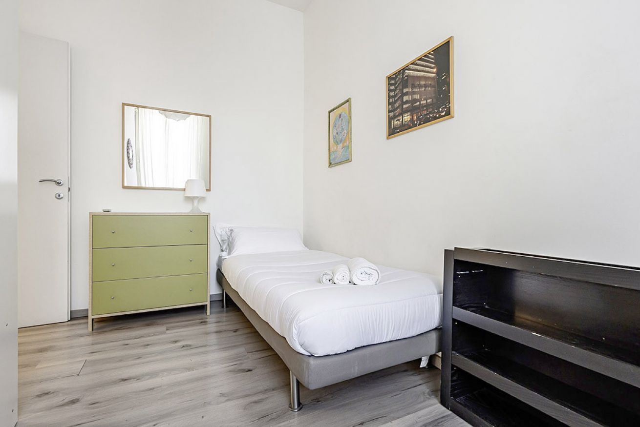 Ein Schlafzimmer mit einem Bett, einem grünen Schminktisch, einem Nachttisch und zwei gerahmten Bildern an der Wand.
