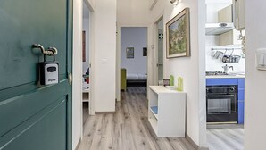 A narrow hallway with a green door on the left, a white door leading to a bedroom, and a kitchen area with a stove and sink on the right. - Coliseum View Diana's House by Rentbeat (Roma)