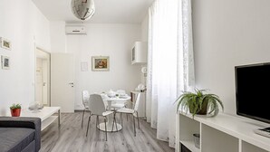 A modern living room with a sofa, a dining table with chairs, a TV, and a potted plant. - Coliseum View Diana's House by Rentbeat (Roma)