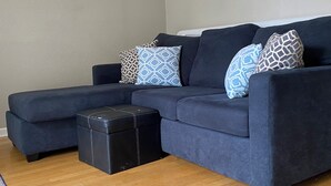 A dark blue sectional sofa with patterned pillows, a black ottoman, and a wooden floor. - Lovely house with WiFi in charming Alameda (Alameda)