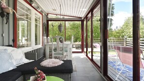 A covered porch with a wicker sofa, a small table with a vase, and a chair.