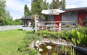 A backyard with a pond, wooden deck, outdoor furniture, and a red building.