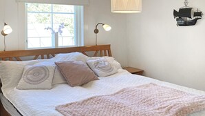 A neatly made bed with a white duvet and a pink throw blanket, a wooden headboard, and two bedside lamps.