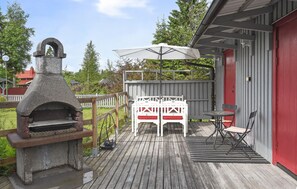 A wooden deck with a stone oven, white chairs, and a table with an umbrella.