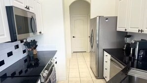 A modern kitchen with white cabinets, a black countertop, a stainless steel refrigerator, and a built-in oven. - Dream Villa W/ Pool Near Disney3 Bed 2 Bath, (Davenport)