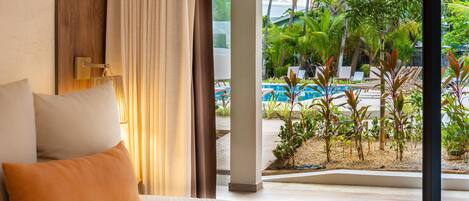 Un dormitorio con cama, cortinas y vistas a una piscina y plantas tropicales.
