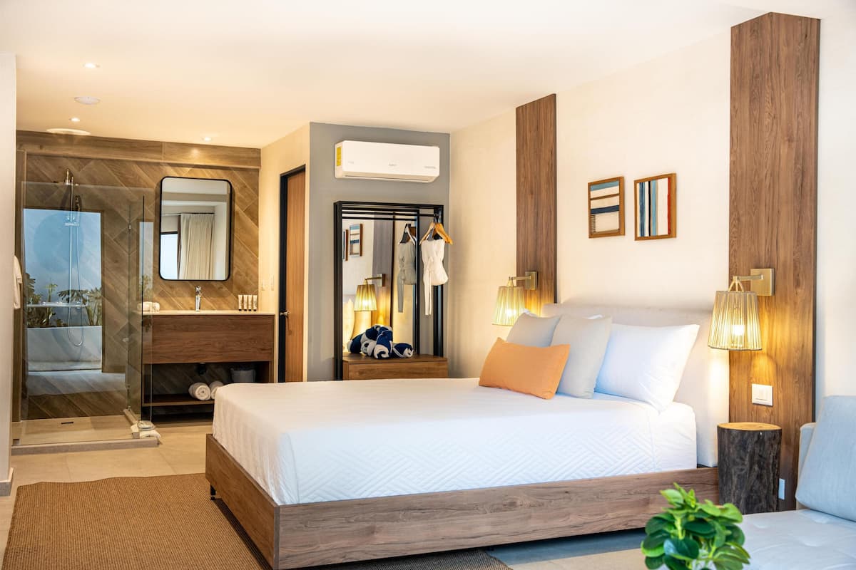 A modern hotel room with a large bed, a bathroom with a glass shower, and a wooden accent wall.