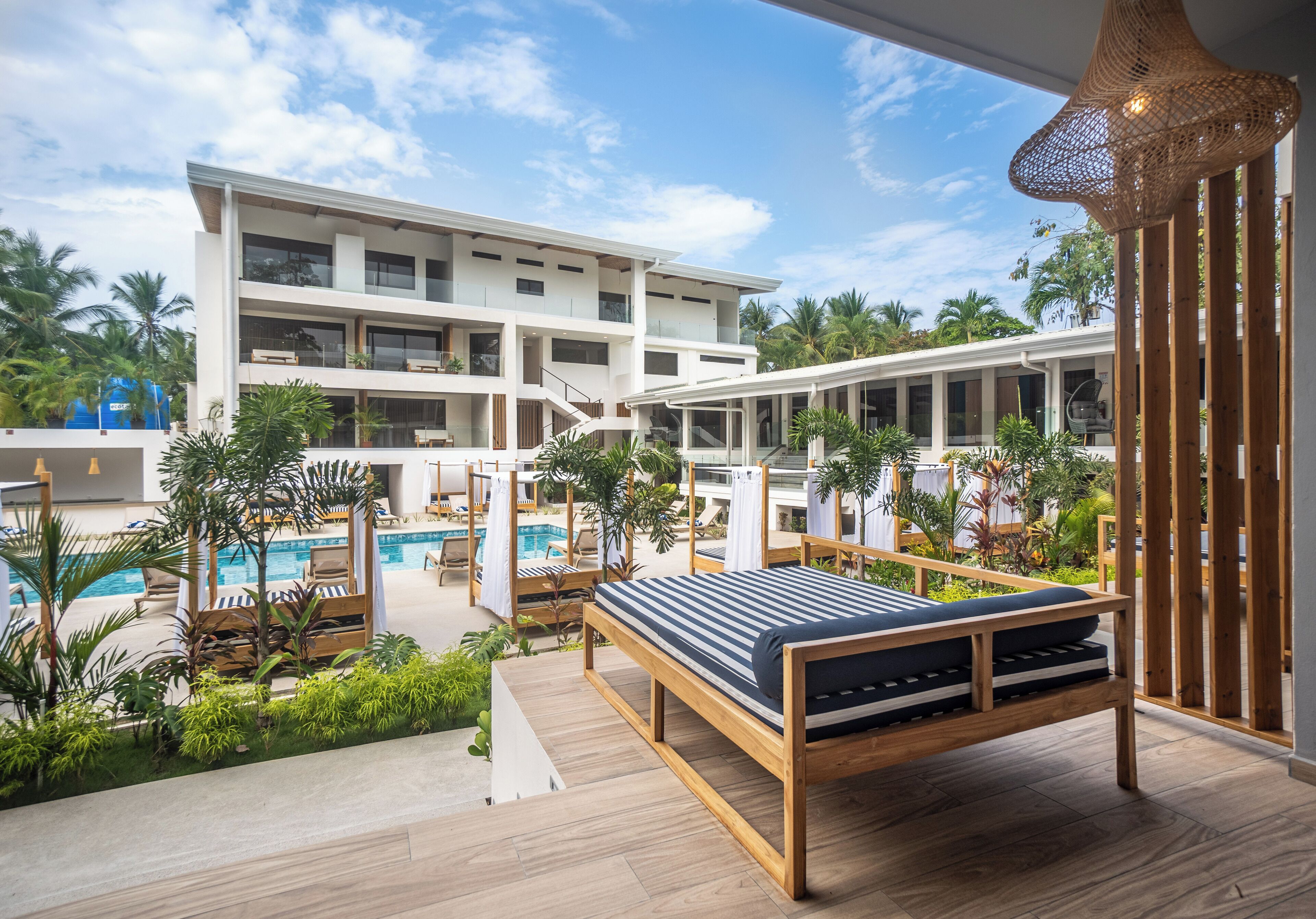 A modern hotel with a pool area, multiple balconies, and lush greenery.