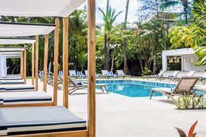 Un espace aménagé au bord de la piscine, avec des chaises longues et une piscine entourée d’une végétation tropicale.
