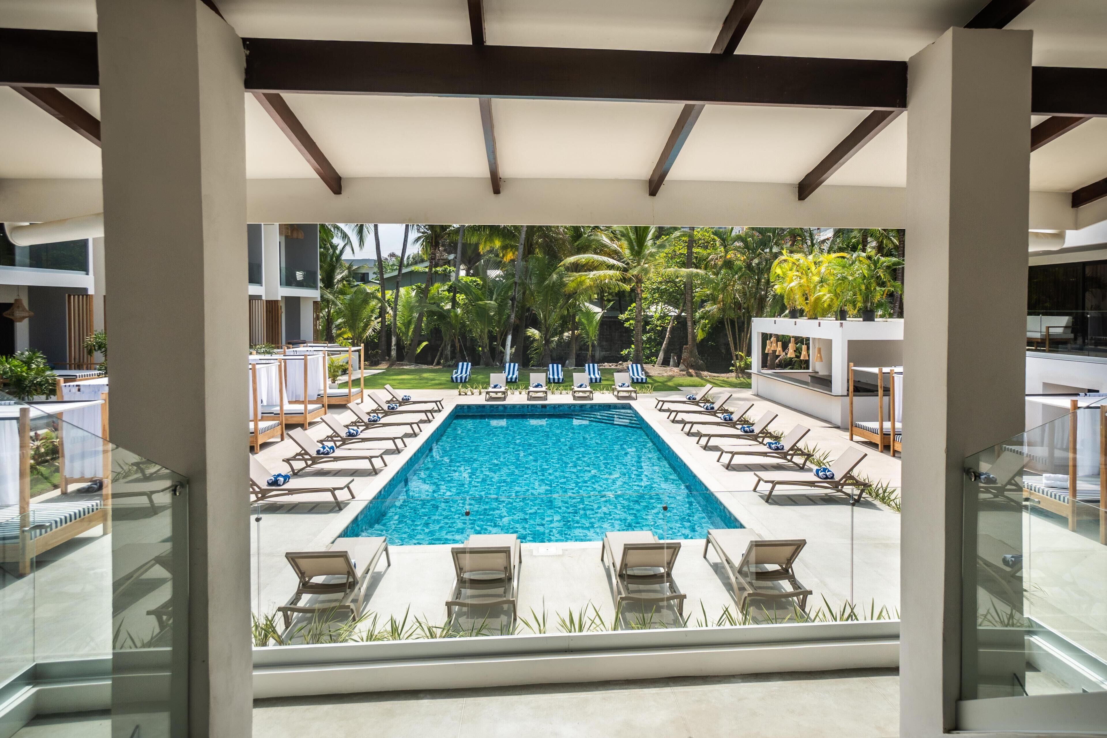 A swimming pool with lounge chairs, surrounded by palm trees and a glass balustrade.