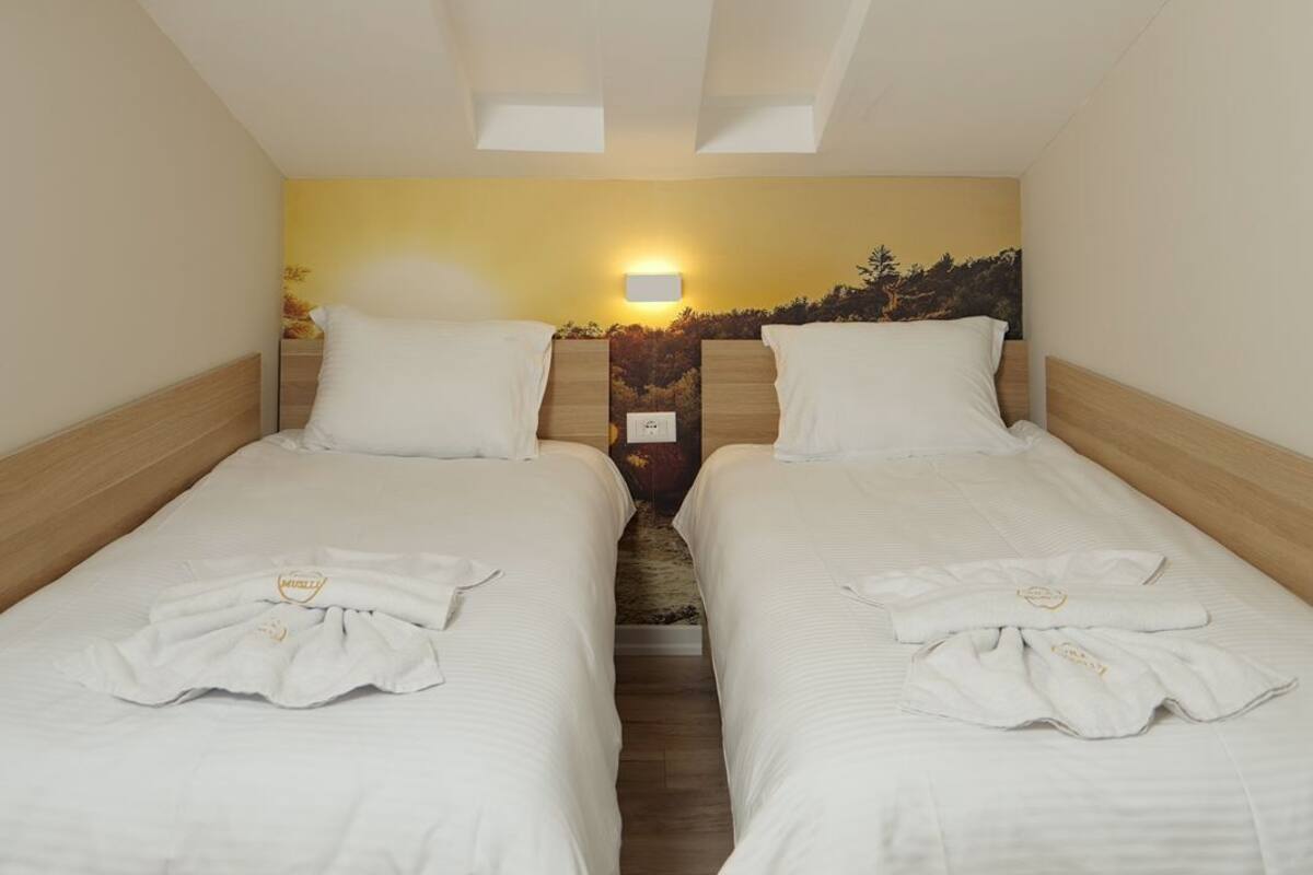 A hotel room with two single beds, a wooden headboard, a wall-mounted light, and a view of a mountainous landscape.
