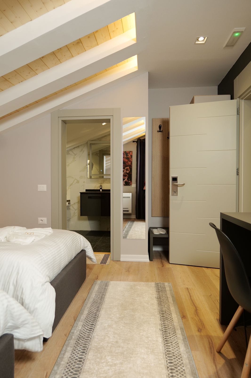 A modern bedroom with a bed, a desk, and a door leading to another room.