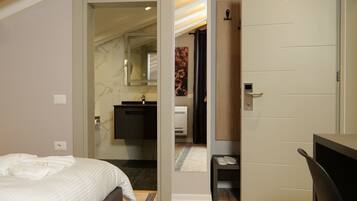 A modern bedroom with a bed, a desk, and a door leading to another room.