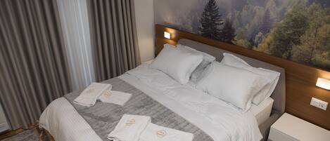 A hotel room with a bed, two bedside tables, a headboard with a forest mural, and a window with curtains.