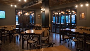 A cozy restaurant with wooden tables and chairs, large windows, and a sign that reads "BEER IS ALWAYS A GOOD IDEA." - Vila Muslli (Korçë)