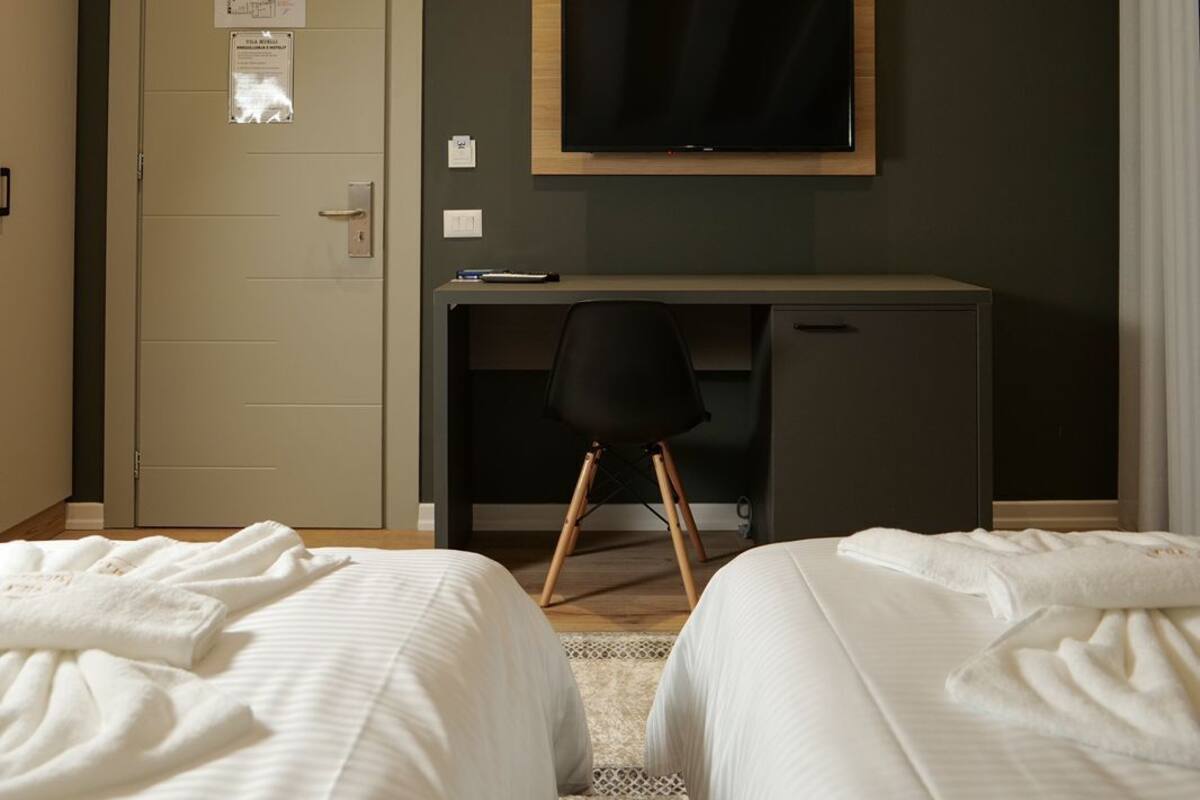 A hotel room with two beds, a desk, a television, and a door with a light switch.
