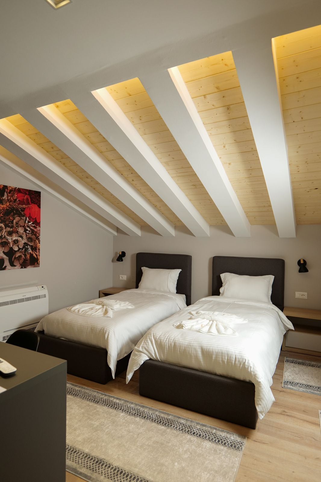 A bedroom with two beds, wooden ceiling beams, and recessed lighting.