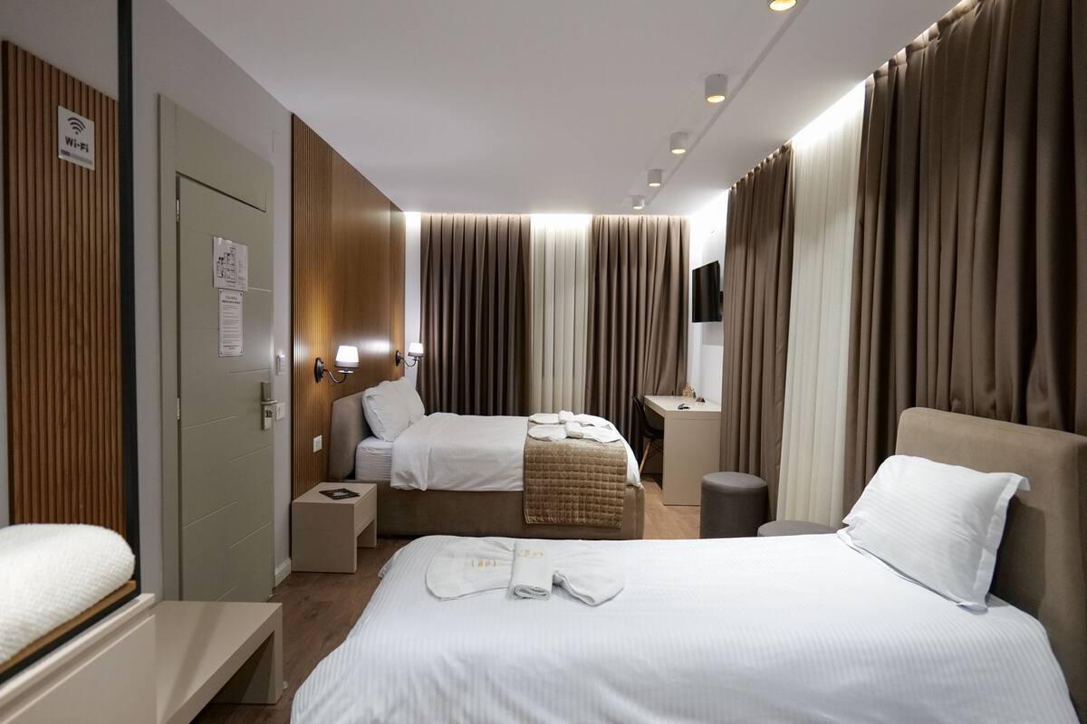 A hotel room with two beds, a desk, and a TV.
