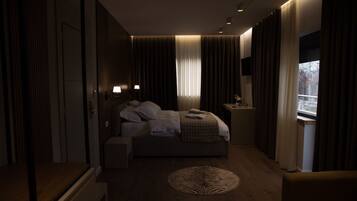 Een moderne hotelkamer met een groot bed, bedlampen, een klein tafeltje en uitzicht op het omliggende landschap door het raam.