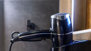 Un sèche-cheveux noir fixé au mur, avec un cordon enroulé.